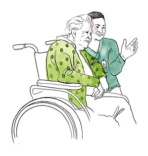Undersköterska hukar sig framför en äldre kvinna i rullstol, ler och håller hennes hand.
