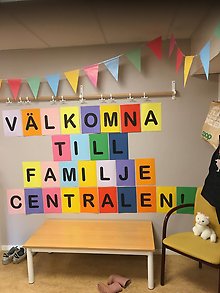 Bild på Familjecentralens hall med färgglada vimplar och texten välkomna till Familjecentralen.