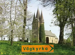 Bild på Husaby kyrka. Längst fram i bild finns en gul skylt med texten "vägkyrka".