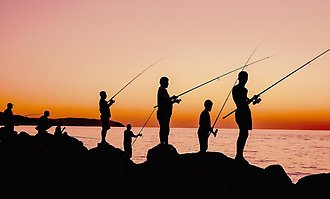 Personer som står och fiskar med orangegul solnedgång.