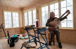 Äldre man sitter med en gitarr i knät som han stämmer.