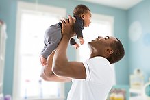 En man lyfter sin bebis upp i luften och ler och tittar på honom.