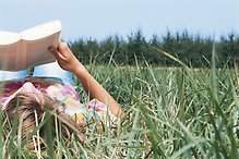 Somrig bild med en läsande ungdom i gröngräset.